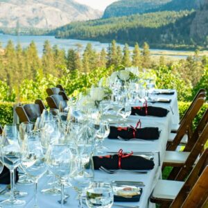 Elegant table setting on white linen with the vines of Noble Ridge and Vaseaux Lake in the background
